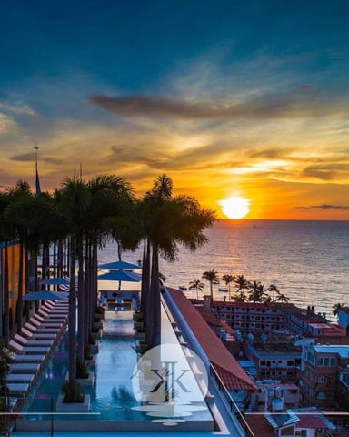 Sunset view from rooftop terrace with palm trees, ocean, and coastal buildings below