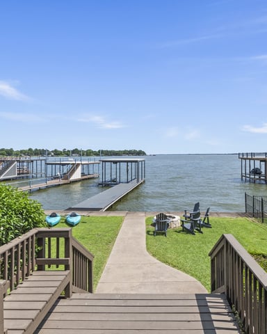 Waterfront property with wooden deck, lawn, boat docks, and Adirondack chairs overlooking calm bay water